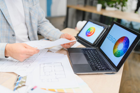 Architect professional developing home design with construction plans, laptop, tablet, and color wheel on the office deskの写真素材