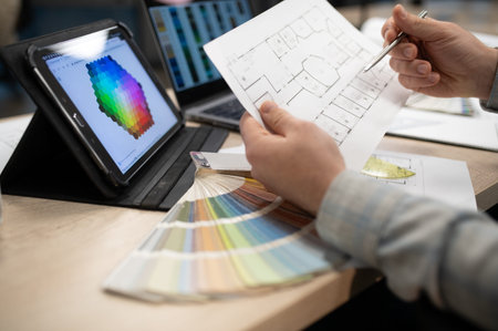 Professional interior designer working on new project, holding architectural blueprints, using a...