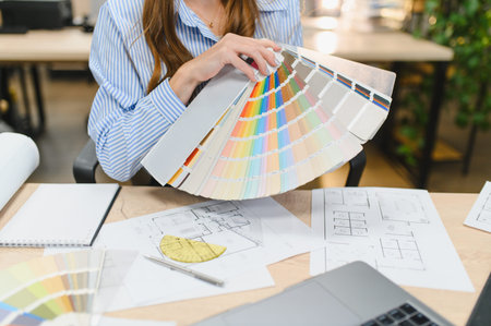 Woman architect or designer holding color swatch palette, studying blueprints and plans on a wooden desk, working on creative projectの写真素材