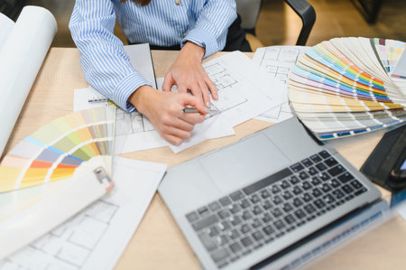 Designer hands drawing blueprints with a ruler, surrounded by color swatches and a laptop, working...