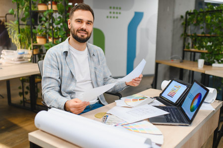 Male professional designer holding documents, working on new project with laptop and color palette...