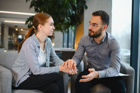 Female patient receiving support from a male psychotherapist during a private therapy session,...