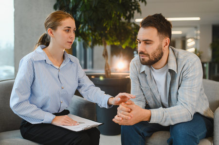 Female psychotherapist comforting a man, offering empathy and support during a counseling session in a modern officeの写真素材