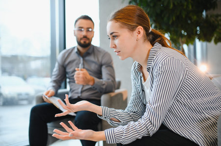 Young woman talking about her problems and emotions during a psychotherapy session with a male...