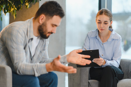 Man talking with female psychotherapist, discussing mental health issues during therapy. Focusing on support and guidanceの写真素材