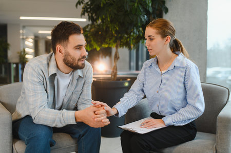 Male patient discussing problems with a caring female psychologist, receiving professional support and mental health therapyの写真素材