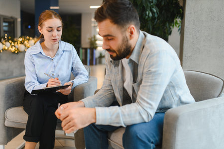 Man discussing problems with professional psychologist, receiving support and counseling for mental health and well beingの写真素材