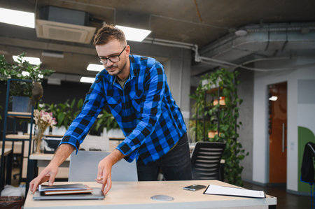 Professional man preparing his desk, opening laptop and organizing documents, ready for work in a...