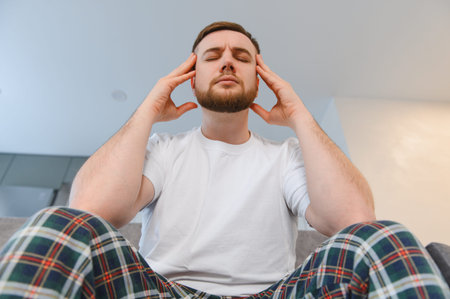 Man experiencing intense head pain, pressing his temples with hands, symbolizing stress, tension, and sicknessの写真素材