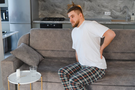 Young man experiencing severe lower back pain at home, needing medication for discomfort and injury...