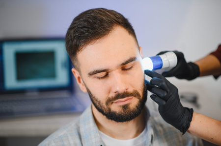 Trichologist in black gloves using a specialized tool to examine a male patient's scalp, checking for hair loss and follicle healthの写真素材