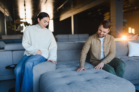 Young man and woman sitting on a comfortable sofa, touching the fabric while shopping for new furniture at a showroomの写真素材