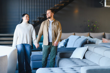 Young couple holding hands, smiling while browsing furniture in a modern showroom, planning home decorの写真素材