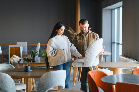 Young couple selecting new dining chairs for their home in a modern furniture store, shopping for home decorの写真素材