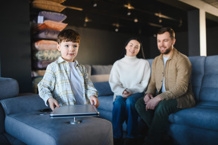 Young boy playing near modern sofa while parents sitting, choosing new furniture for home,...
