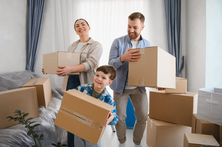 Young family, parents and son, smiling and carrying cardboard boxes, getting ready to unpack in their new homeの写真素材