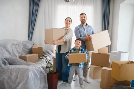 Family smiling and carrying cardboard boxes in bright new apartment, celebrating moving day and the...
