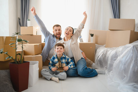Excited family with child celebrating successfully moving into a new house, surrounded by cardboard...