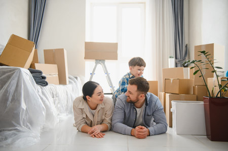 Happy family lying on the floor in their new apartment, surrounded by cardboard boxes after moving...