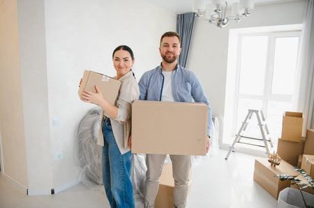 Young couple carrying cardboard boxes, relocating into their new apartment, starting fresh in a...
