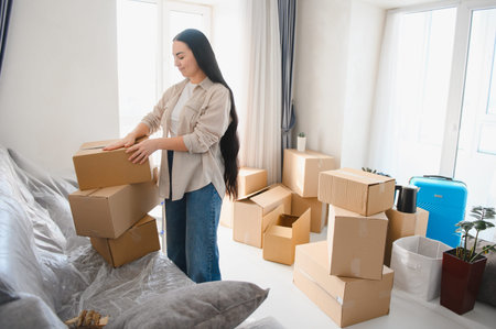 Happy woman settling into her new apartment, surrounded by cardboard moving boxes. Relocation and home ownership conceptの写真素材