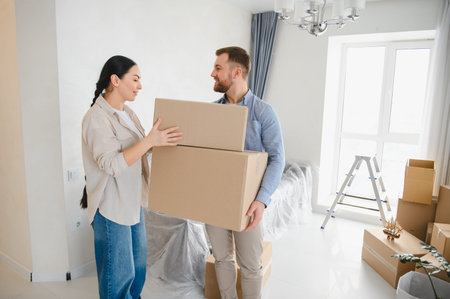 Young couple collaborating, carrying moving boxes into their new empty apartment, celebrating relocation and property ownershipの写真素材