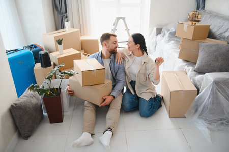 Happy couple celebrating new home ownership, sitting on floor surrounded by moving boxes and...