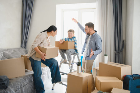Happy family with child carrying cardboard boxes, unpacking belongings in new apartment. Relocation...