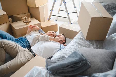 Young couple smiling, lying on the floor surrounded by moving boxes, feeling relieved and content...