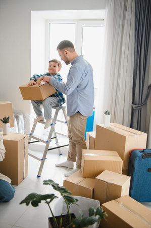 Happy father and son enjoying relocation day, sitting on a stepladder and opening cardton boxes in their new apartmentの写真素材