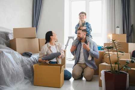 Family unpacking belongings in their new apartment. Father giving son a piggyback ride while mother...