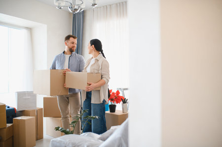 Happy couple holding cardboard boxes, moving into new house or flat. Lifestyle scene of relocation...