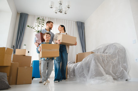 Parents and son carrying cardboard boxes and a houseplant, relocating to a new house, starting a new...