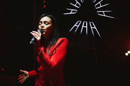 Female performer in a red dress singing passionately into a microphone during a live concert in a...
