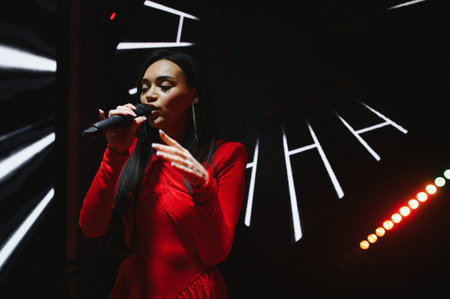 Woman in red dress singing into a microphone on a dark stage, experiencing a live musical...