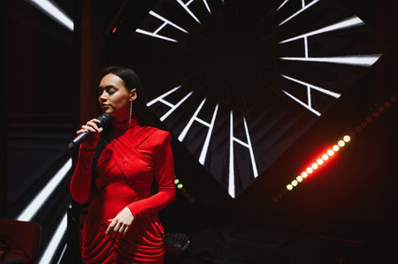 Young woman in red dress holding microphone, singing on stage with dynamic lighting and abstract...