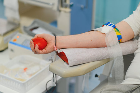 Person donating blood in a medical clinic, holding a red stress ball to facilitate the process, supporting healthcareの写真素材