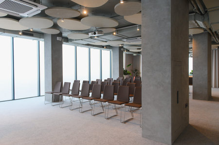 Empty chairs arranged in rows inside a modern conference room, featuring industrial design elements...
