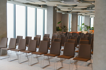 Rows of brown chairs set up in a bright, contemporary convention space with large windows, ready for...