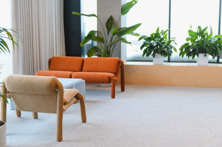 Modern interior space featuring an orange sofa, light beige armchair, and numerous potted green...