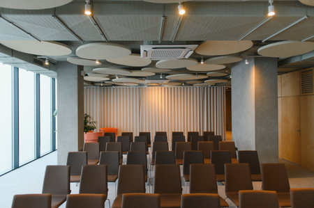 Modern conference room interior with rows of empty chairs, acoustic ceiling design, and large...