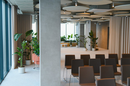 Contemporary event space displaying rows of dark chairs and lush green plants, creating a modern and...