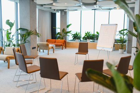 Conference room with chairs arranged in a circle, a flipchart, and green indoor plants creating a...
