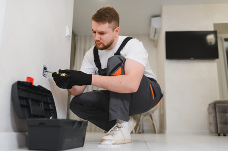 Professional electrician working on electrical repairs, using a screwdriver to install a new power...