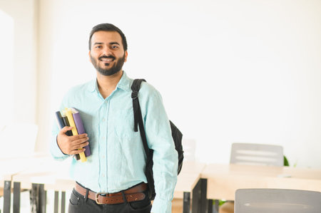 Indian male student smiling and carrying textbooks, ready for classes at a modern university or college campus