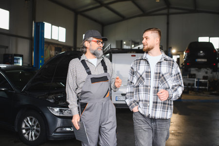 Experienced auto mechanic discussing vehicle repair with a young male client, offering professional car maintenance advice in a garage