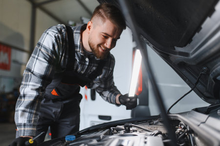 Young male mechanic smiling while working on a car engine, performing diagnostics and maintenance in an auto repair shop