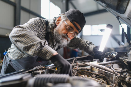 Experienced auto mechanic performing vehicle diagnostics, illuminating the car engine with a lamp during a service inspection