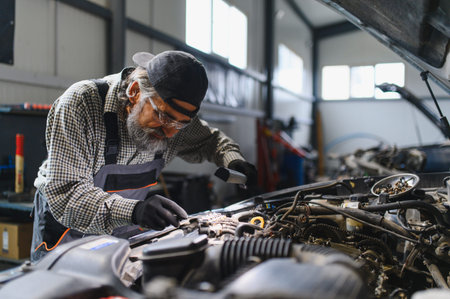 Experienced auto mechanic examining a vehicle engine with a flashlight during repair and maintenance service in a workshop