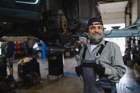 Experienced auto mechanic standing in a service workshop, holding tools and smiling, ready for car repair and maintenance
